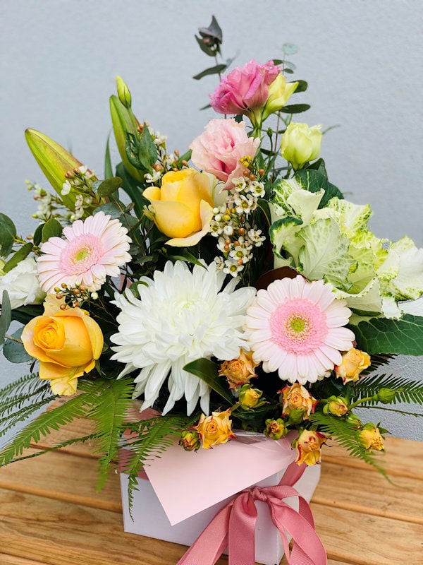 Box flowers arrangement on wooden table, white box with pink bow ribbon and pink paper