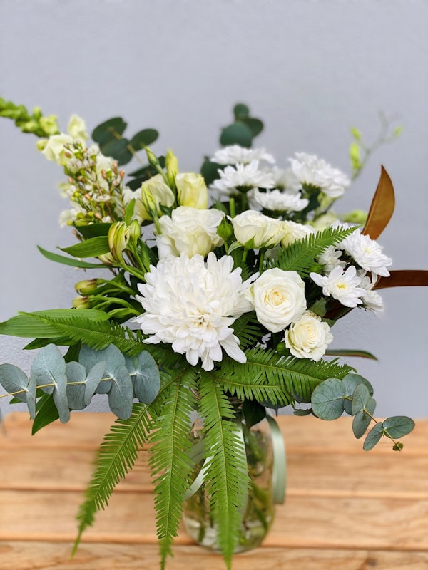 Vase flowers arrangement on wooden table, white flowers and greenery