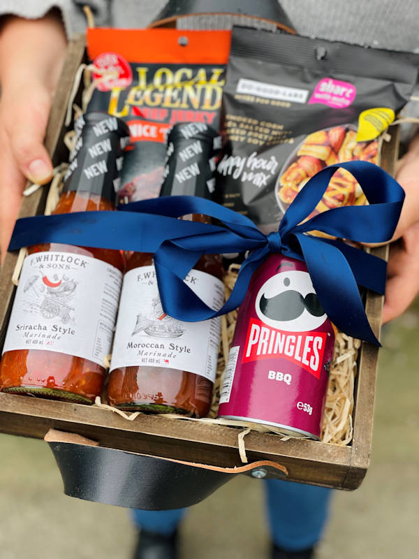 BBQ lovers hamper with beef jerky, snacks, and bottles of marinade in a wooden crate